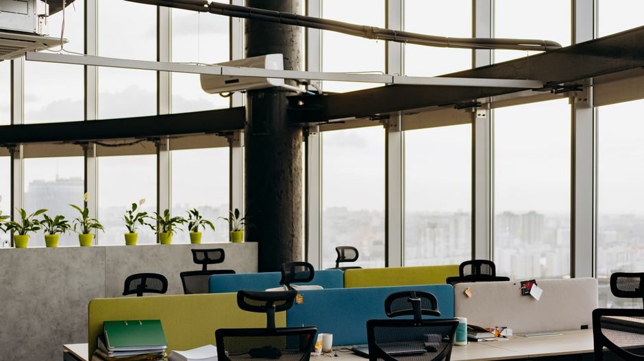A spacious open office with colorful dividers, large windows, and a cityscape view, perfect for creative work environments.